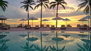 schöner luxusschirm und stuhl rund um den außenpool mit kokospalme am sonnenuntergangs- oder sonnenaufgangshimmel - urlaubs- und urlaubskonzept