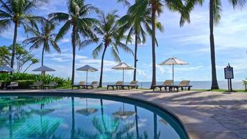 Beautiful luxury umbrella and chair around outdoor swimming pool with coconut palm tree on sunset  or sunrise sky - holiday and vacation concept video