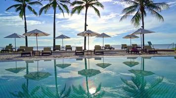 Beautiful luxury umbrella and chair around outdoor swimming pool with coconut palm tree on sunset  or sunrise sky - holiday and vacation concept video