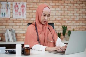 Portrait of a beautiful female doctor, beautiful Muslim in uniform with a stethoscope, smiling and working with laptop in hospital's clinic. One person who has expertise in professional treatment. photo