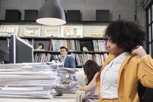 Busy female worker, young African American staff is hard working with a lot of stack of documents and paperwork on desk, overload worked tirelessly for the job deadline in business office workspace. photo