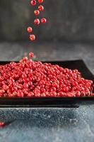 Pour red peppercorns on top of plate of pepper photo