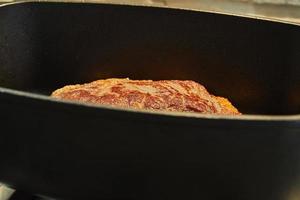 large piece of beef is fried in special cauldron on gas stove photo