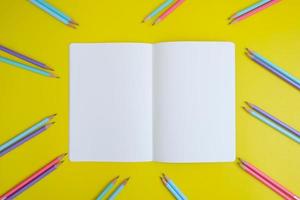 Blank notebook, a pencil, and space are on top of a yellow office desk table. Flat lay, top view education concept photo