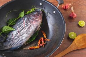 pescado fresco en una sartén y especias para cocinar foto