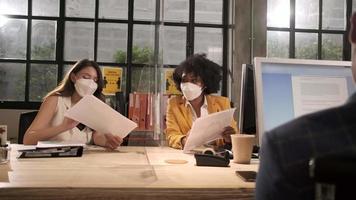 Two female coworkers team with face mask working in new normal office. COVID-19 protection by cleared partition, business workplace office, social distancing for pandemic health, disease prevention. video