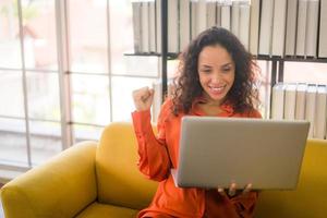 Mujer latina que trabaja con el portátil en el sofá con sentimiento feliz foto