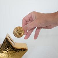 Woman hand with a bitcoin, aproaching a golden piggy bank photo