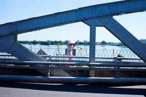 Unrecognizable person going to the market with a conical straw hat and a carrying pole. Crossing the Hue bridge. Vietnam photo