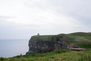 Cliffs at Moher on a rainy day. Green fields and ancient tower.Ireland