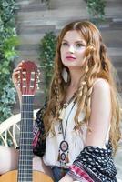 A beautiful girl with red curly hair sits on a chair with a seven-string guitar. photo