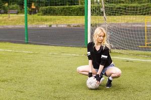 la niña está sentada en el campo de fútbol con la pelota. foto