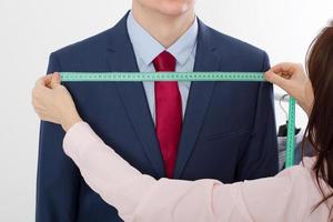 Closeup image of tailor taking measurements for business jacket suit. Businessman in red tie and blue suit at studio isolated on white background. photo