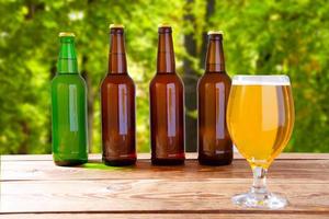 Taza de cerveza y botellas en caja de madera en la mesa en el fondo del parque borrosa foto