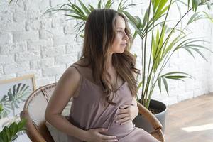 Pregnant girl sitting in a chair on a white background.