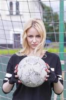 hermosa rubia con una pelota en la portería de fútbol. foto