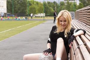 The girl sits on the bench at the football field with the ball. photo