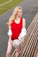 Girl football player stands with the ball at the bench in red. photo