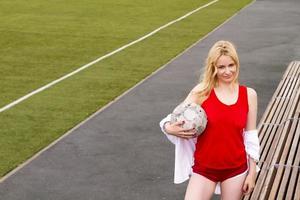 Blonde with a ball on the football field in red uniform.