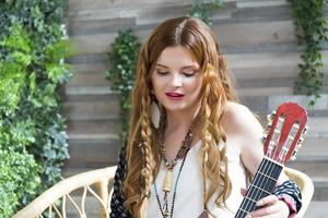 A beautiful girl with red curly hair sits on a chair with a seven-string guitar. photo