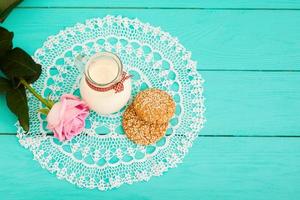 Oat flakes and cookies with jug of milk on blue wooden kitchen. Tablecloth in polka dots. Copy space and selective focus photo