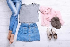 Modern outfit with different accessories and female legs in jeans on white wooden floor. Top view and copy space. photo