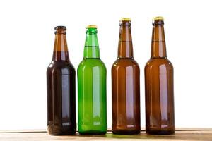 Photo of four different full beer bottles with no labels. Separate clipping path for each bottle included. Four 4 separate photos merged together. Beer bottles on wooden table isolated