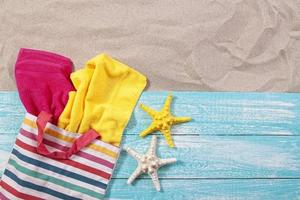 Beach bag with towels on wooden board on sand top view copy space photo