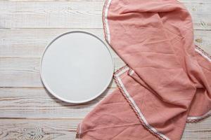Empty white plate and pink towel at wooden table. View from above, copy space. photo
