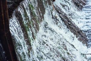 Water rapidly flows in a cascade along the concrete wall of the dam. Dam. photo