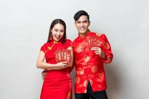 Happy Asian couple in traditional oriental costumes holding red envelopes or Ang Pao in light gray background for Chinese new year concepts,  texts mean great luck great profit photo