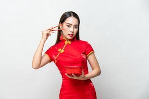 Beautiful Asian woman in traditional red Chinese qipao dress holding food box and chopsticks in studio isolated gray background
