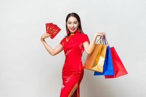 Portrait of smiling happy Asian woman carrying colorful bags and showing red envelopes for Chinese new year shopping concepts, text means great luck great profit