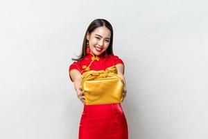 Happy smiling Asian woman in traditional costume giving gold gift box in light gray isolated studio background for Lunar new year concepts photo