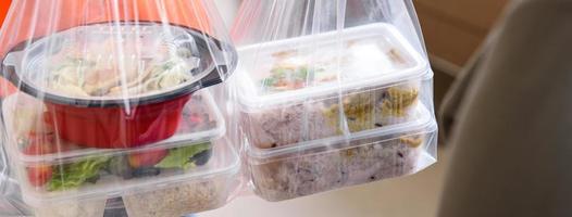 Panoramic banner image of Asian food boxes in plastic bags delivered to customer at home by delivery man photo