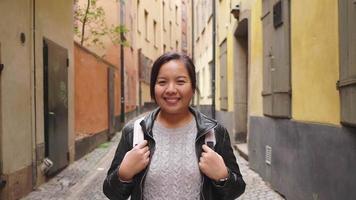 vista frontale di una donna asiatica felice in piedi e sorridente per strada in città, uscendo per una passeggiata per strada in svezia. viaggiare all'estero in vacanza lunga. guardando il concetto di fotocamera video