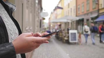 close-up handen van aziatische vrouw die staat en smartphone gebruikt in de stad, wandelen op straat in zweden. op lange vakantie naar het buitenland video