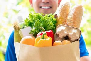 Smiling delivery man holding a grocery bag ready to deliver to the customer at home photo