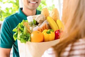 Smiling delivery man giving grocery bag to woman customer at home for online food shopping service concept photo