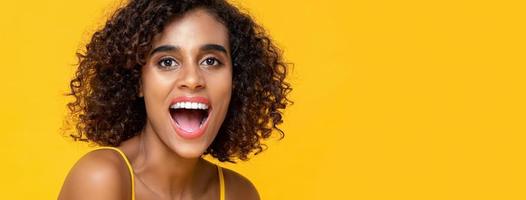 Close up portrait of happy African American woman looking at camera with mouth open in isolated studio yellow banner background
