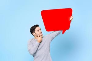 Young handsome caucasian man thinking and looking up to empty red speech bubble isolated on light blue background photo