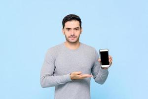 Handsome Caucasian man showing mobile phone with empty screen isolated on light blue background photo