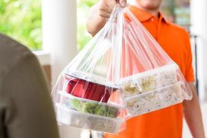 repartidor dando comida en las bolsas al cliente que ordenó en línea en casa foto