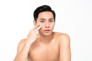 Handsome young Asian man touching under eye skin isolated on white background for beauty concepts photo