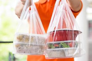 cajas de comida asiática en bolsas de plástico entregadas al cliente en casa por un repartidor con uniforme naranja foto