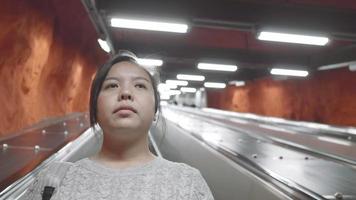 vista frontal de una mujer asiática parada en una escalera mecánica, mirando a un lado y pensando en algo. tomar el transporte público para llegar a casa. viajar solo al extranjero