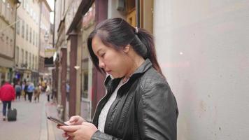 donna asiatica in piedi e utilizzando lo smartphone in città, camminando per strada in svezia. viaggiare all'estero in vacanza lunga. un sacco di gente che cammina per strada video
