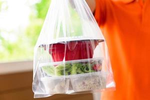 cajas de comida asiática en bolsas de plástico entregadas al cliente en casa por un repartidor con uniforme naranja foto