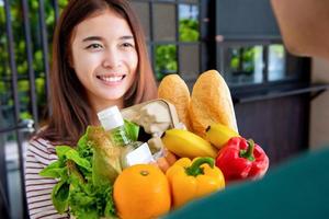 Smiling Asian woman getting food and grocries from delivery man at home photo