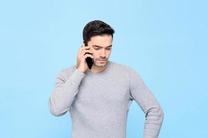 Portrait of serious and upset handsome Caucasian man calling on cellphone with unhappy facial expression in isolated studio blue background photo